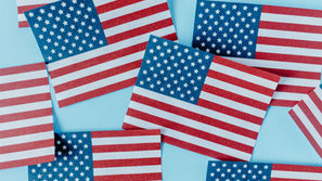 Small paper copies of the American Flag scattered across a blue background.