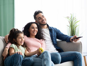 Photo of a family with a dad, mom, and child sitting on a couch smiling while watching TV