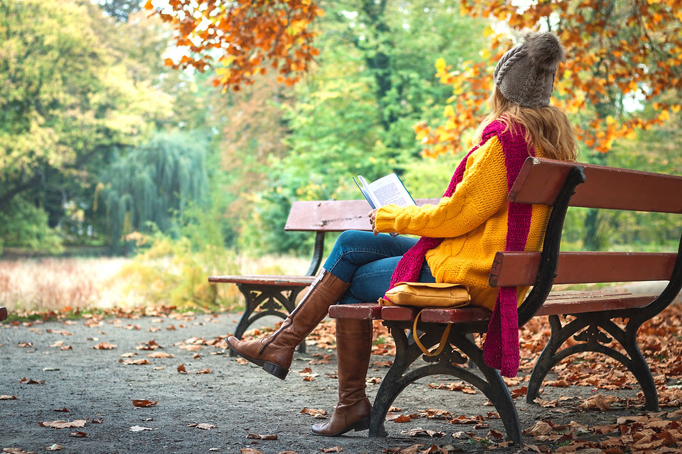 Woman sitting on a park bench with a book wearing an orange sweater and a beanie in an autumn setting