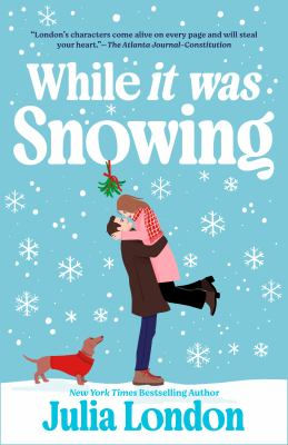 Couple embraces under mistletoe in snowy scene; dog in red coat nearby. Book title "While it was Snowing" by Julia London.