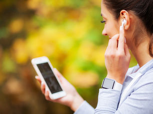 Young woman with earbud checks her phone against a blurred golden autumn background.