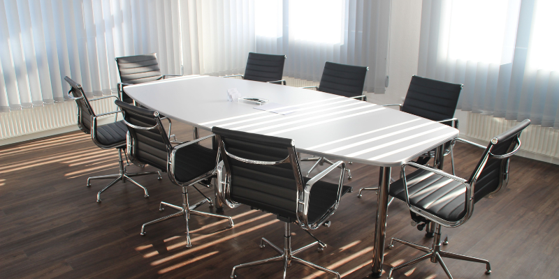 Sunlit conference room with white meeting table, black swivel chairs, and papers on the table, empty and tidy.